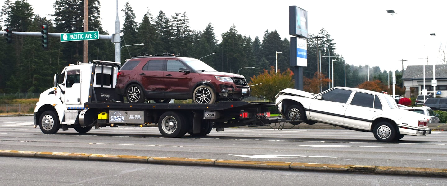 Oblačný deň, odťahovka vezie poškodené SUV a sedan.
