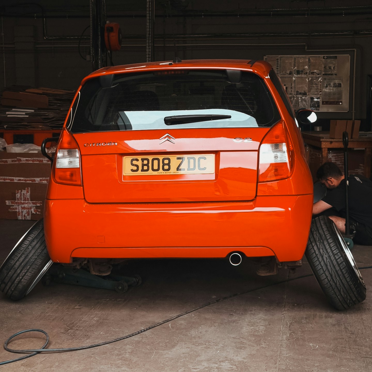 Mechanik opravuje oranžové auto zdvihnuté na zdviháku v dielni.