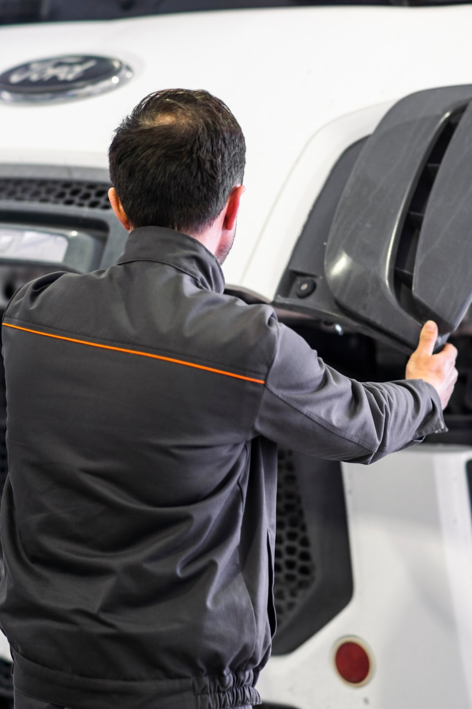 Mechanik kontroluje veľký motorový priestor vozidla, drží sivý panel.