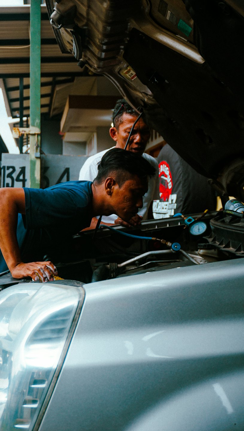 Dvaja mechanici spoločne kontrolujú motor auta pod kapotou.